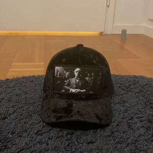 Svart velvet keps (aldrig använd helt ny) - Snygg svart keps med ett tryck av en man i kostym på framsidan. Kepsen har ett nätmaterial på baksidan för bättre ventilation och en justerbar rem för perfekt passform.