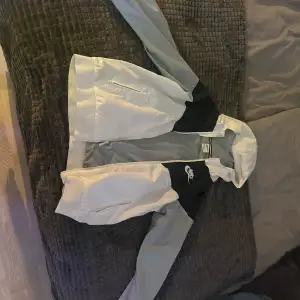 Säljer en stilren svart och vit vindjacka från Nike. Jackan har dragkedja och är perfekt för blåsiga dagar. Den har långa ärmar och en klassisk design med Nike-logga på bröstet.