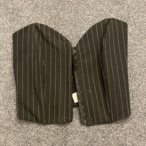 Svart randig korsett - Snygg svart korsett med vita ränder och hakknäppning fram. Storlek XS! Passar bra till både fest och vardag!