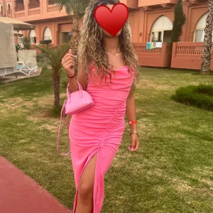 Rosa midiklänning med slits - Trendig rosa klänning med smala axelband och en snygg slits framtill. Klänningen har en åtsittande passform och rynkdetaljer som ger en extra touch. Har dessutom ”inbyggd bh” .Perfekt för sommarens alla tillfällen. 