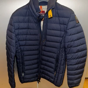 Mörkblå pufferjacka från Parajumpers - Snygg mörkblå pufferjacka (super lightweight) från Parajumpers med dragkedja och hög krage, k perfekt skick. Storlek Small. Jackan har en quiltad design och är perfekt för kyligare väder. Den har en diskret logga på ärmen och praktiska fickor med dragkedja. Nypris på Care of Carl ligger på 5199kr. Säljs för 2200kr