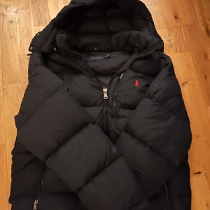  Ralph Lauren Jacka - Snygg svart dunjacka från Polo Ralph Lauren med huva och dragkedja. Jackan  är perfekt för kyligare väder. Storlek L men passar nog M också. 
