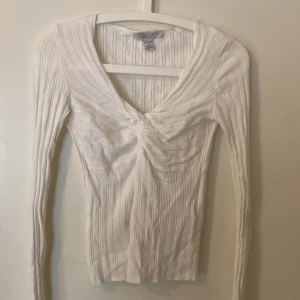 Vit ribbad topp från Amisu - Säljer en stilren vit ribbad topp från Amisu med knytning framtill. Toppen har långa ärmar och en v-ringad design som ger en elegant touch. Perfekt för att skapa en chic look.