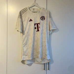 Vit fotbollströja från Adidas - Säljer en stilren vit fotbollströja från Adidas med korta ärmar och snygga detaljer i rött. Perfekt för fotbollsfans som vill ha en bekväm och snygg tröja att bära både på och utanför planen. Tredje tröja 23/24