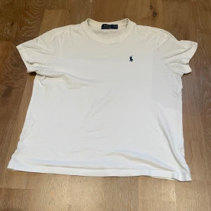 Vit t-shirt från Ralph Lauren - Säljer en klassisk vit t-shirt från Ralph Lauren med det ikoniska broderade logotypen i blått på bröstet. Perfekt för en stilren look. Tröjan har storlek M men passar S
