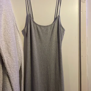 Grå ärmlös klänning med smala axelband - Snygg grå klänning med smala axelband och en enkel design. Perfekt för en avslappnad stil. Klänningen har en rak passform och är tillverkad i ett mjukt material.