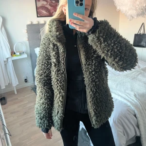 Grön teddyjacka - Mysig grön teddyjacka med dragkedja framtill. Perfekt för kyliga dagar med sin fluffiga och varma design. Jackan har en normal passform och långa ärmar.