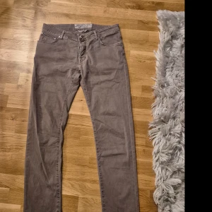 Gråbruna  jeans från Jacob Cohën - Snygga gråbruna jeans från Jacob Cohën, handgjorda i Italien. De har en klassisk femficksdesign och en knappgylf. Perfekta för en stilren look.