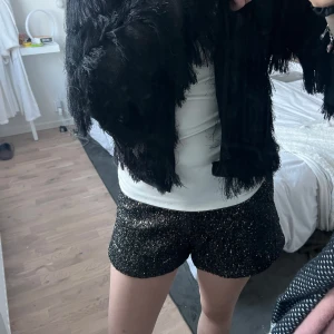 Svarta glittriga shorts - Snygga svarta shorts med glittrig yta, perfekta för en festlig look. De har en bekväm passform och är ett måste för garderoben när du vill sticka ut.