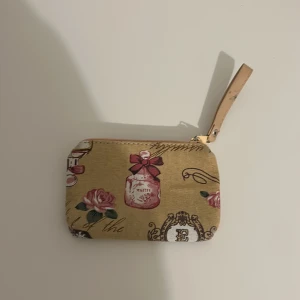 Beige plånbok med fina detaljer🎀 - Charmig beige plånbok med jättefina detaljer som parfymflaskor och fjärilar. Den har en praktisk dragkedja och en liten rem för enkel hantering. Perfekt för att hålla ordning på småsaker i väskan.💗använd en gång,priset kan diskuteras🎀🎀