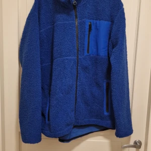 Blå fleecejacka från 157 - Säljer en mysig blå fleecejacka från 157. Jackan har en dragkedja framtill och praktiska fickor med dragkedjor. Perfekt för kyliga dagar.