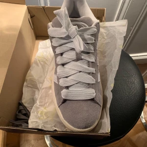 Grå Adidas Campus 00s sneakers - Snygga grå Adidas Campus 00s sneakers med vit sula och klassiska tre ränder på sidan. Skorna har en bekväm passform och är perfekta för vardagsbruk. De har en gummisula med bra grepp och snörning för justerbar passform.  38 och 2/3 är storleken jag tänkte förlänge och 14 dagar retur försvann jag behöver en storlek större  Skorna är helt oanvända  
