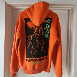 Orange hoodie med coolt tryck🧡 - Säljer en cool orange hoodie med tryck på ryggen och en streckkod på framsidan. Hoodien har en stor ficka framtill och en bekväm passform. Perfekt för en avslappnad stil😁 Från Lisa Anckarmans kollektion med madlady.
