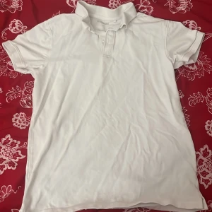 Vit pikétröja från Kappahl - Säljer en klassisk vit pikétröja från Kappahl i storlek M. Tröjan har korta ärmar och en traditionell krage med knappar. Perfekt för en stilren och avslappnad look.