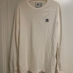 Vit långärmad tröja från Adidas - Säljer en stilren vit långärmad tröja från Adidas med det klassiska logotyptrycket på bröstet och ryggen. Perfekt för en avslappnad look.
