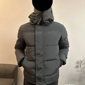 Grå dunjacka från Canada Goose - Helt ny grå dunjacka från Canada Goose med huva och dragkedja. Originalpåse och taggar medföljer.