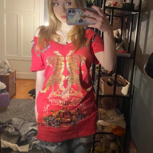 Röd t-shirt från Christian Audigier❤️ - Snygg röd t-shirt från Christian Audigier(villket ägs av samma företag som Ed Hardy) med ett unikt tryck av tigrar, rosor och vingar. T-shirten har en v-ringad hals och korta ärmar❤️ de står den är L men skulle säja att den sitter mer som en M 