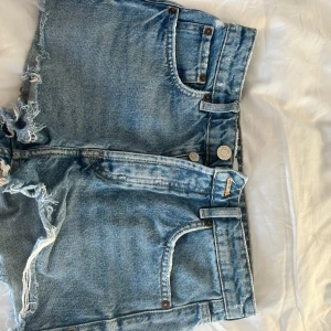 Blå jeansshorts från Zara - Säljer ett par snygga blå jeansshorts från Zara med fransiga kanter och klassisk femficksdesign. Perfekta för en avslappnad sommarlook🩷