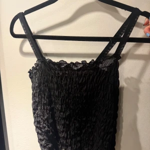 Svart linne från NA-KD - Snygg svart linne  från NA-KD med smockdetaljer och smala axelband. Perfekt för en stilren look. Tillverkad i ett lätt och bekvämt material.