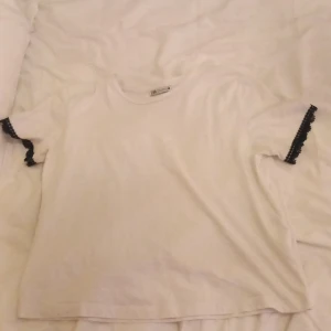 Vit t-shirt från Zara med spetsdetaljer - Jätte fin vit t-shirt från zara med svarta spets detaljer på ärmarna. I storlek M men passar även S skulle jag säga!💗