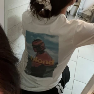 Vit t-shirt med Frank Ocean tryck - Vit t-shirt med ett färgglatt tryck på ryggen med Frank Ocena/ blond. T-shirten har en normal passform och korta ärmar, perfekt för en avslappnad stil.