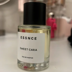 Essnce Sweet Cara Eau de Parfum - En elegant flaska med Essnce Sweet Cara Eau de Parfum. Doften kommer i en stilren, genomskinlig glasflaska med en svart kork. Perfekt för den som söker en söt och lockande doftupplevelse.