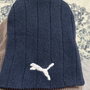 Mörkblå ribbad mössa från Puma - Snygg mörkblå mössa från Puma med ribbad design och broderad logga framtill. Perfekt för kyliga dagar.
