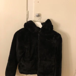 Svart teddyjacka från H&M - Mysig svart teddyjacka från H&M med dragkedja framtill. Perfekt för kyliga dagar med sin fluffiga och varma design. Jackan har en hög krage och långa ärmar för extra komfort.