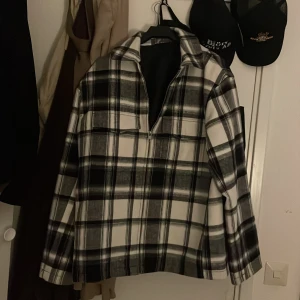 Svartvit rutig jacka med dragkedja - Snygg svartvit rutig jacka med dragkedja framtill. Jackan har en klassisk krage och långa ärmar, perfekt för en stilren look. Passar bra till både vardag och mer avslappnade tillfällen.