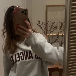 Grå sweatshirt med Los Angeles-tryck - Säljer en grå sweatshirt med texten 'Los Angeles' i mörk färg på bröstet. 