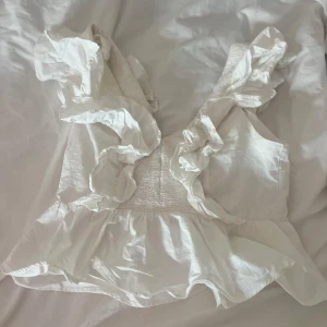 Vit blus med volangdetaljer - Säljer en söt vit blus med volangdetaljer och djup v-ringning.💗 Jätte fint skick och knappt använd. Stl 36 (jag är XS, 34/36, ca 163cm)