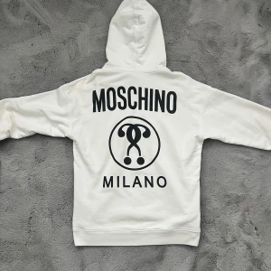 Vit hoodie från Moschino - Riktigt snygg vit hoodie från Moschino med stor logga på ryggen och mindre logga på bröstet. Perfekt för en stilren och avslappnad look.                                           Köpt på Farfetch, kvitto finns!                                                 