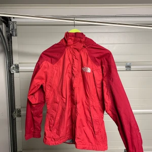 Röd vindjacka från The North Face - Säljer en röd vindjacka från The North Face i bra skick. Jackan har en justerbar huva och dragkedja framtill. Perfekt för blåsiga dagar och utomhusaktiviteter. Den är lätt och smidig att ha med sig. Passar bra för både vår och höst. Säljes i befintligt skick. Storlek: S