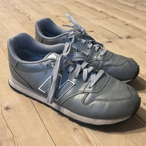 Grå sneakers från New Balance - Säljer ett par grå New Balance 500 sneakers i bra skick. De har en klassisk design med snörning och en bekväm passform. Perfekta för vardagsbruk eller lätt träning. Sulan är i bra skick och de är riktigt sköna att gå i. Passar både till jeans och träningskläder.