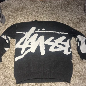 Svart och vit stickad tröja från Stüssy - Säljer en cool svart och vit tröja från Stüssy med ett stort grafiskt mönster på framsidan. Tröjan har långa ärmar och en rund halsringning. Funkar som M och L i passform och använd 1-2 gånger max 