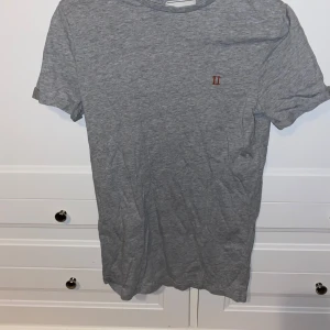 Grå t-shirt från Les Deux - Snygg grå t-shirt från Les Deux med en liten broderad logga på bröstet. Perfekt för en avslappnad stil. Tillverkad i mjukt material för extra komfort.