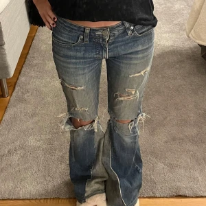 Blå bootcut jeans med slitningar - Säljer ett par blå bootcut jeans med coola slitningar på framsidan. De har en låg midja och väldigt snygga. Några slitningar bak vid rumpan men inget man tänker på.