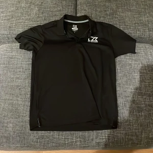 Svart pikétröja från Cutter & Buck - Säljer en stilren svart pikétröja från Cutter & Buck i storlek S. Tröjan har korta ärmar och en klassisk krage med knappar. Perfekt för både vardag och lite mer uppklädda tillfällen. Materialet känns mjukt och bekvämt. Passar bra till både jeans och chinos! Pris går alltid att förhandlas!