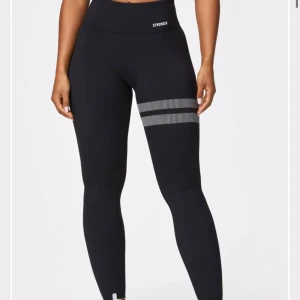Svarta leggings från Stronger - Snygga svarta leggings från Stronger med hög midja och ett stilrent randigt mönster på ena benet. Perfekta för träning eller en aktiv vardag. Använda lite men väldigt bra skick🫶