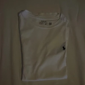 Vit t-shirt från Ralph Lauren - Säljer en klassisk vit t-shirt från Ralph Lauren med den ikoniska broderade loggan på bröstet. T-shirten är kortärmad och tillverkad i mjuk bomull, perfekt för en stilren look.