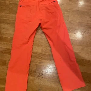 Orange skidbyxor från J.Lindeberg - Säljer ett par snygga orange skidbyxor från J.Lindeberg i storlek M. Dessa är fodrade och gjorda i ett vattentåligt material med flertalet funktionsfickor och ventilations dragkedjor! Nypris 3000kr använda 2 ggr