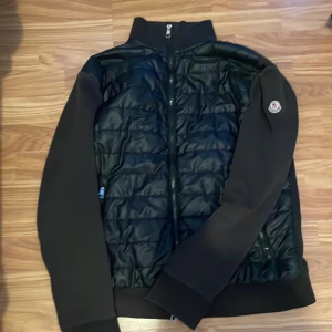 Moncler cardigan  - Snygg svart cardigan från Moncler med quiltad framsida och dragkedja. Jackan har långa ärmar och en stilren design, perfekt för kyligare dagar. Cardigan har några defekter som går att se på bilderna. Skick 7/10 den är i storlek S men passar även som storlek M.