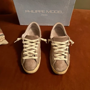 Beige sneakers från Philippe Model - Snygga beige sneakers från Philippe Model med vita snören och en kontrasterande svart detalj på sidan. Skorna har en klassisk design med en bekväm sula och är perfekta för en stilren look.