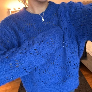 Blå stickad tröja - Säljer en snygg blå stickad tröja med ett luftigt mönster. Tröjan har långa ärmar och en rund halsringning, perfekt för kyligare dagar. Den är både stilren och bekväm, ett måste i garderoben!