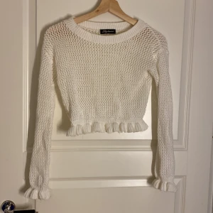 Vit stickad croppad tröja - Säljer en söt vit stickad tröja. Den är croppad med volangdetaljer vid nederkanten och ärmsluten.