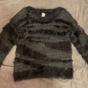 Svart fluffig tröja från H&M - Mysig svart tröja från H&M i storlek M. Den har en fluffig textur med glittriga detaljer som ger en festlig känsla. Perfekt för kyliga dagar när du vill vara både varm och stilren. Passar bra till både vardag och fest!
