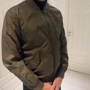 Olivgrön bomberjacka - Säljer en snygg olivgrön bomberjacka i mycket bra skick. Jackan har en dragkedja framtill och långa ärmar med muddar. Perfekt för höst och vår, och ger en cool look till vardagsoutfiten. Passar bra till både jeans och chinos. Passar S/M storlek