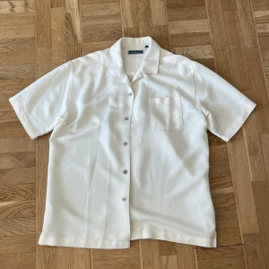 Vit kortärmad skjorta  - Säljer en stilren, krämvit kortärmad skjorta från Cubavera. Skjortan har en klassisk krage och knappar framtill. Lätt och luftig design. 