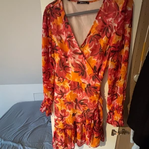 Blommig omlottklänning från Gina Tricot - Snygg blommig omlottklänning i rött och orange från Gina Tricot. Klänningen har långa ärmar och volangdetaljer vid fållen. Perfekt för sommaren!! Finns ej att köpa längre