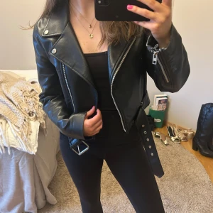Svart skinnjacka Zara - Snygg skinnjacka med klassisk bikerstil. Jackan har en croppad passform och har lite slitning vid ärmarna, annars inga defekter! 